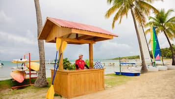 A wooden beach kiosk with a red roof, surrounded by palm trees and a beach view.