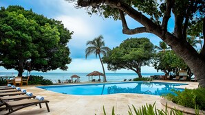 A pool area with lounge chairs, a palm tree, and a view of the ocean. - Copamarina Beach Resort & Spa (Guanica)