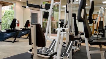 Un gimnasio con diversas máquinas de ejercicio, suelo de colchonetas negras y vistas al exterior con vegetación.