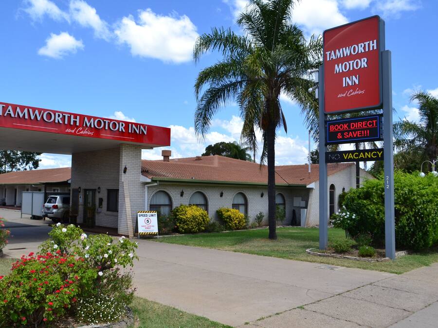 A motel with a red sign, a speed limit sign, and a 'No Vacancy' sign.