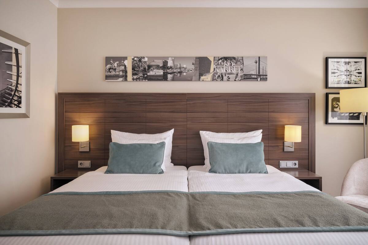 Una cama doble con dos almohadas, cabecera con una obra de arte urbana y dos lámparas de noche.