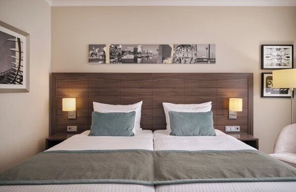 A double bed with two pillows, a headboard with a cityscape artwork, and two bedside lamps.
