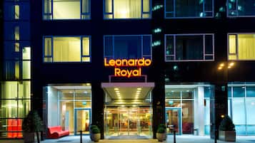 Ein Hotel mit Eingangsbereich, einer auffälligen Neonreklame, Glastüren und einer roten Sitzgelegenheit außen.