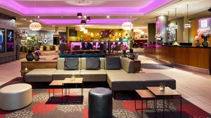 Eine moderne Lobby mit Sitzgelegenheiten, einem Empfangsbereich und einer Bar- oder Lounge-Ecke.