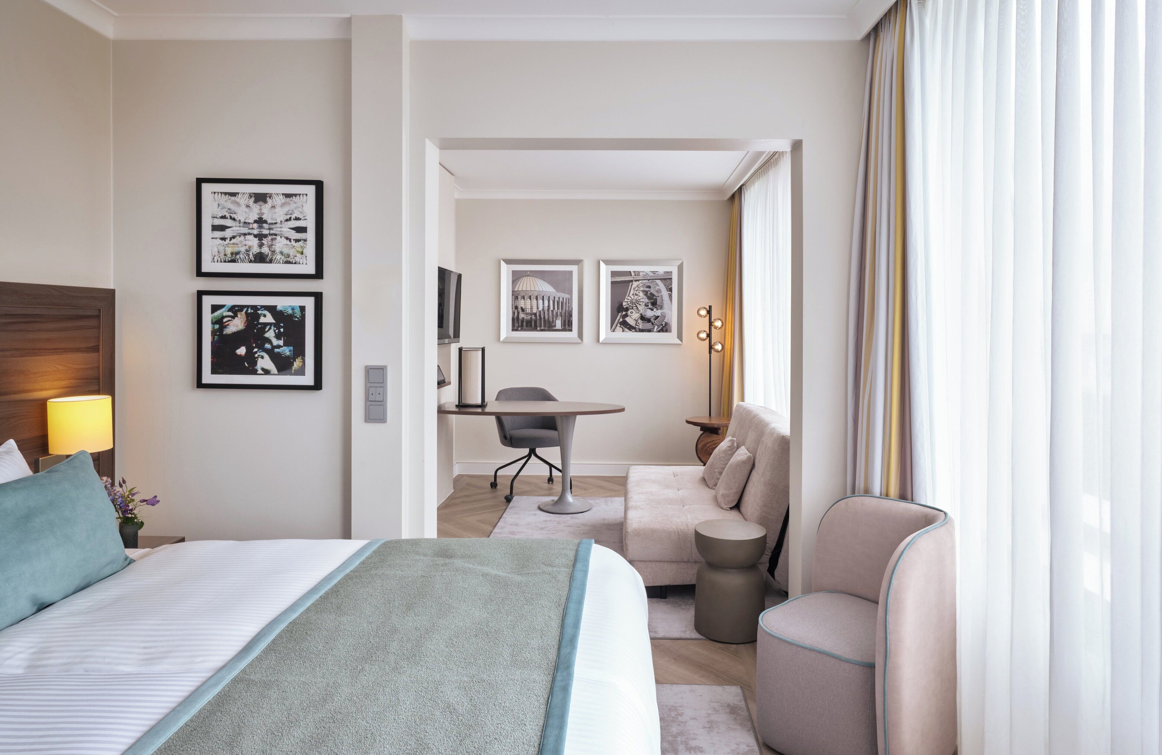 Habitación de hotel con cama, escritorio, sofá y sillón. En la pared hay cuadros enmarcados y una lámpara en la mesita de noche.