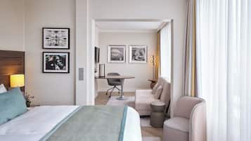 Habitación de hotel con cama, escritorio, sofá y sillón. En la pared hay cuadros enmarcados y una lámpara en la mesita de noche.