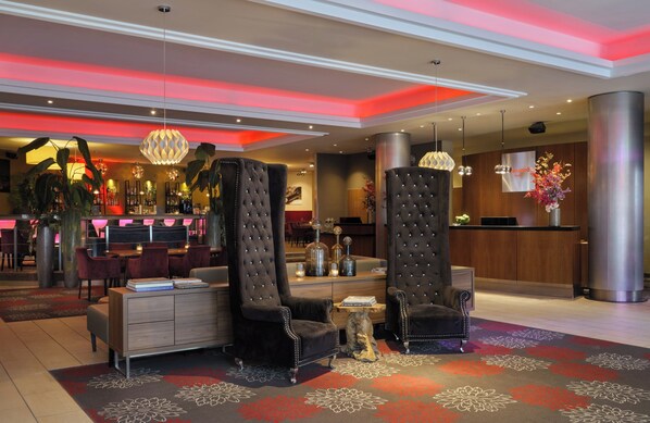 A modern hotel lobby with a reception desk, seating area, and a bar.