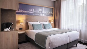 Ein modernes Hotelzimmer mit einem großen Bett, zwei Nachttischen mit Lampen, einem Holzschrank und einem Wandbild mit Stadtansicht.