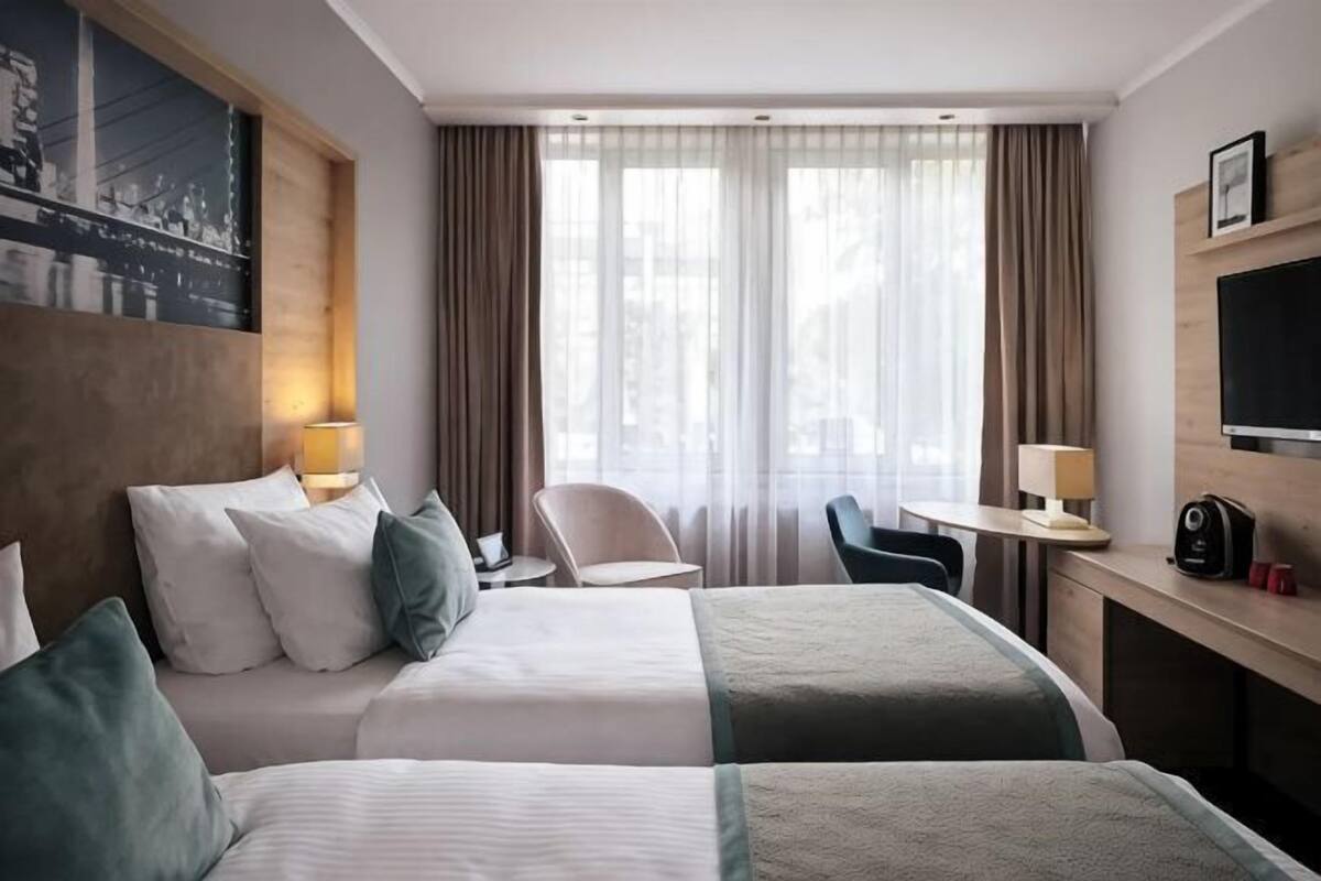 Habitación de hotel con dos camas, un escritorio, una silla, un televisor y una ventana con cortinas.