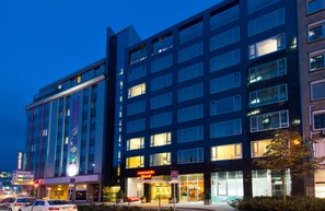 Un hôtel à plusieurs étages, doté d’une façade moderne, de fenêtres illuminées et d’une enseigne hôtelière bien visible.