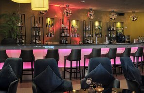 A bar area with multiple seating options, a variety of bottles on shelves, and decorative lighting fixtures.