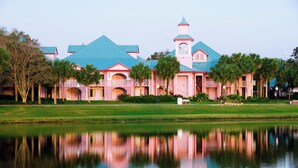 A large, pink and blue building with a central tower, surrounded by a pond and palm trees. - Disney's Caribbean Beach Resort (Lake Buena Vista)