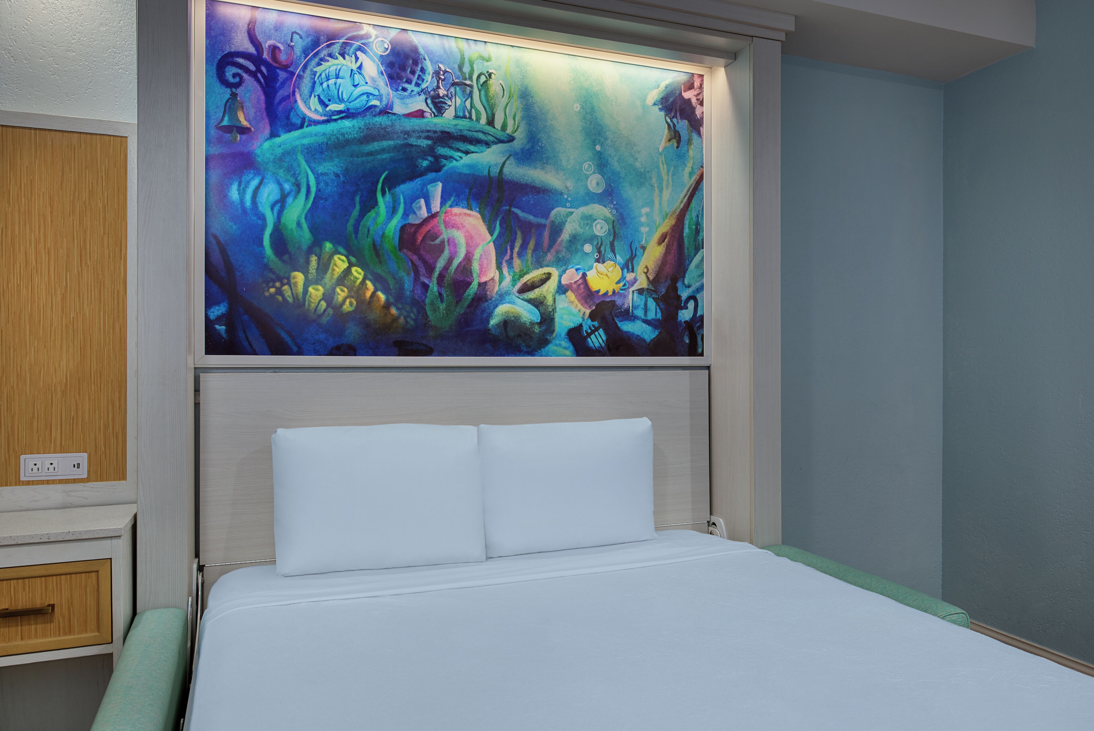 A hotel room with a bed, a nightstand, and a wall-mounted painting of an underwater scene.