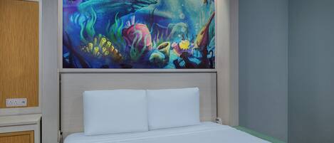 A hotel room with a bed, a nightstand, and a wall-mounted painting of an underwater scene.