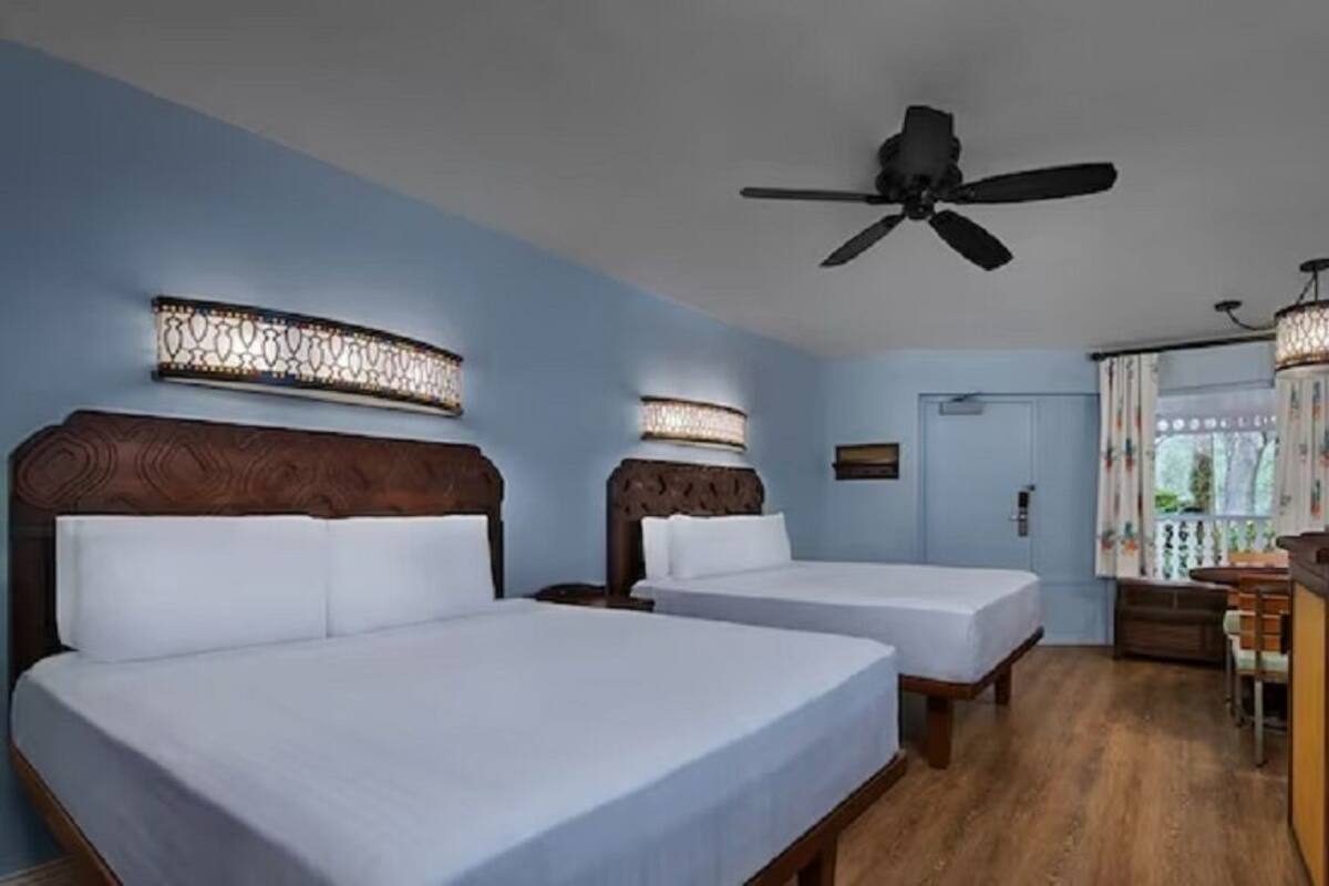 A hotel room with two beds, a ceiling fan, a desk with a chair, and a TV.