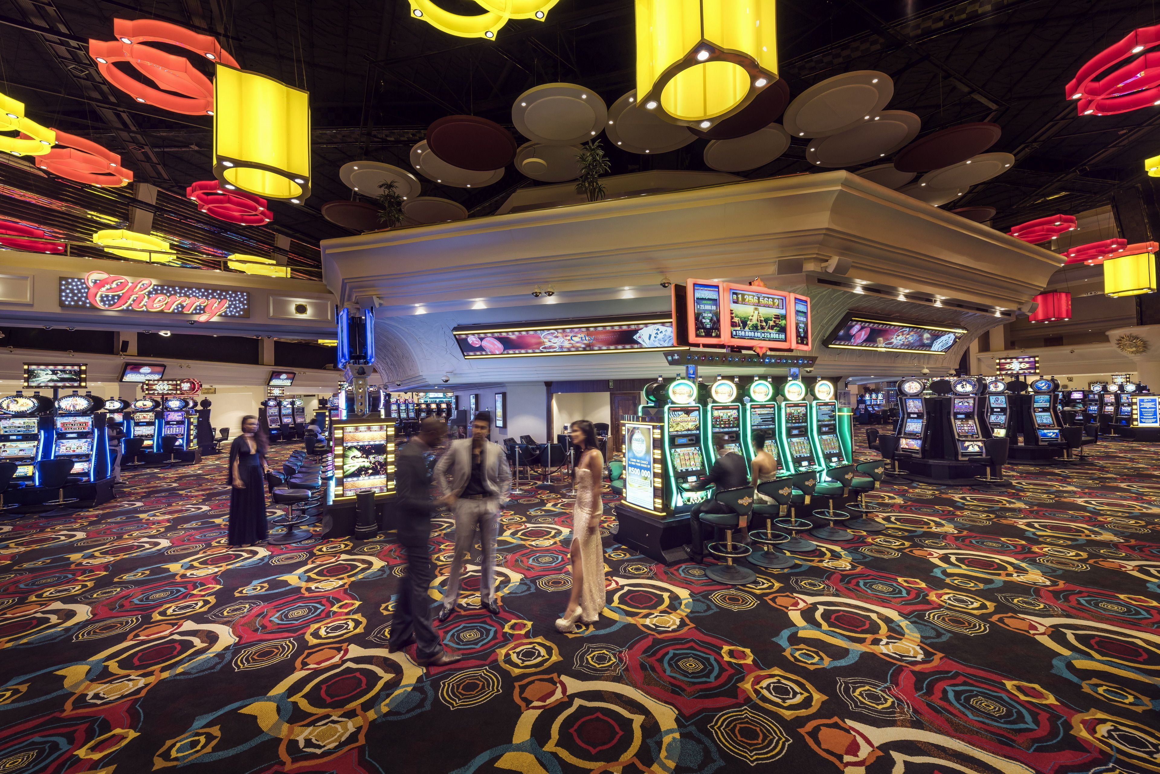 A casino with multiple slot machines, a large chandelier, and a patterned carpet.