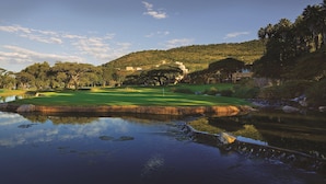 A golf course with a pond reflecting the landscape, surrounded by trees and hills. - The Cascades Hotel at Sun City Resort (Moses Kotane)