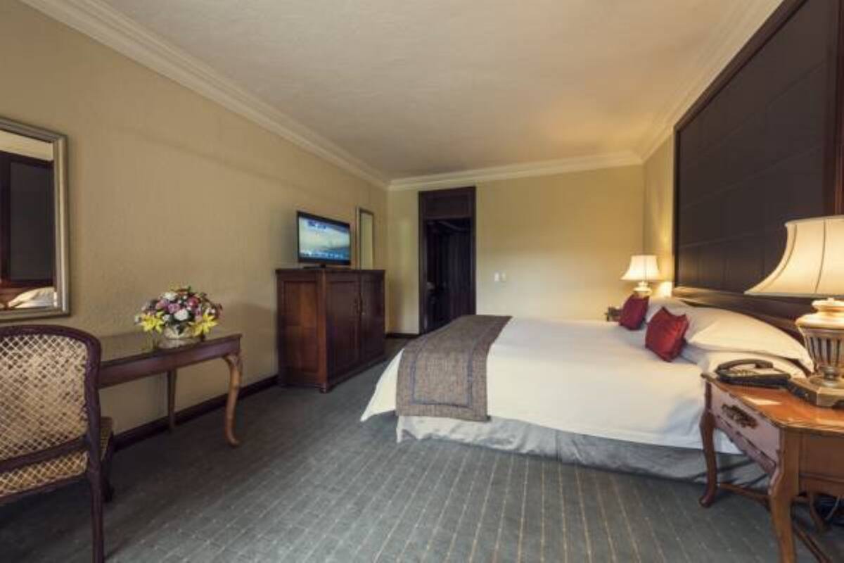 Une chambre d’hôtel comprenant un lit, une table de chevet, une lampe, une chaise et un téléviseur posé sur un meuble.