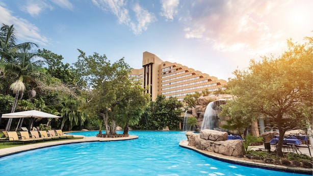 A resort pool with lounge chairs, a waterfall feature, and a large building in the background. - The Cascades Hotel at Sun City Resort (Moses Kotane)