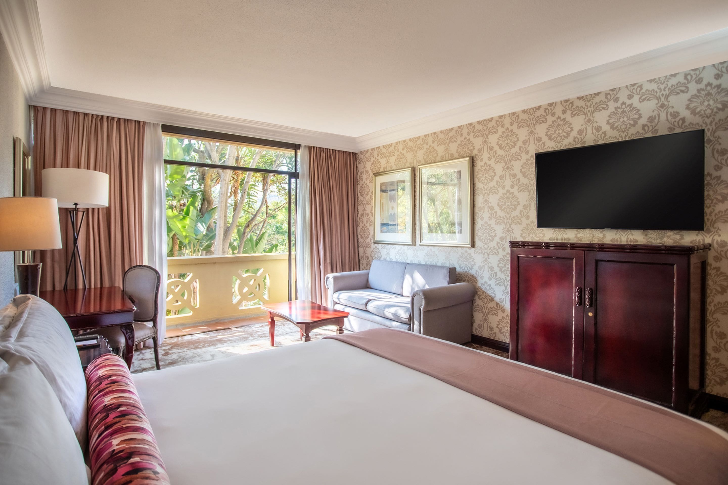 Habitación de hotel con una cama grande, un sofá, un televisor, un escritorio y una ventana con cortinas.