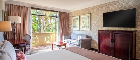 Habitación de hotel con una cama grande, un sofá, un televisor, un escritorio y una ventana con cortinas.