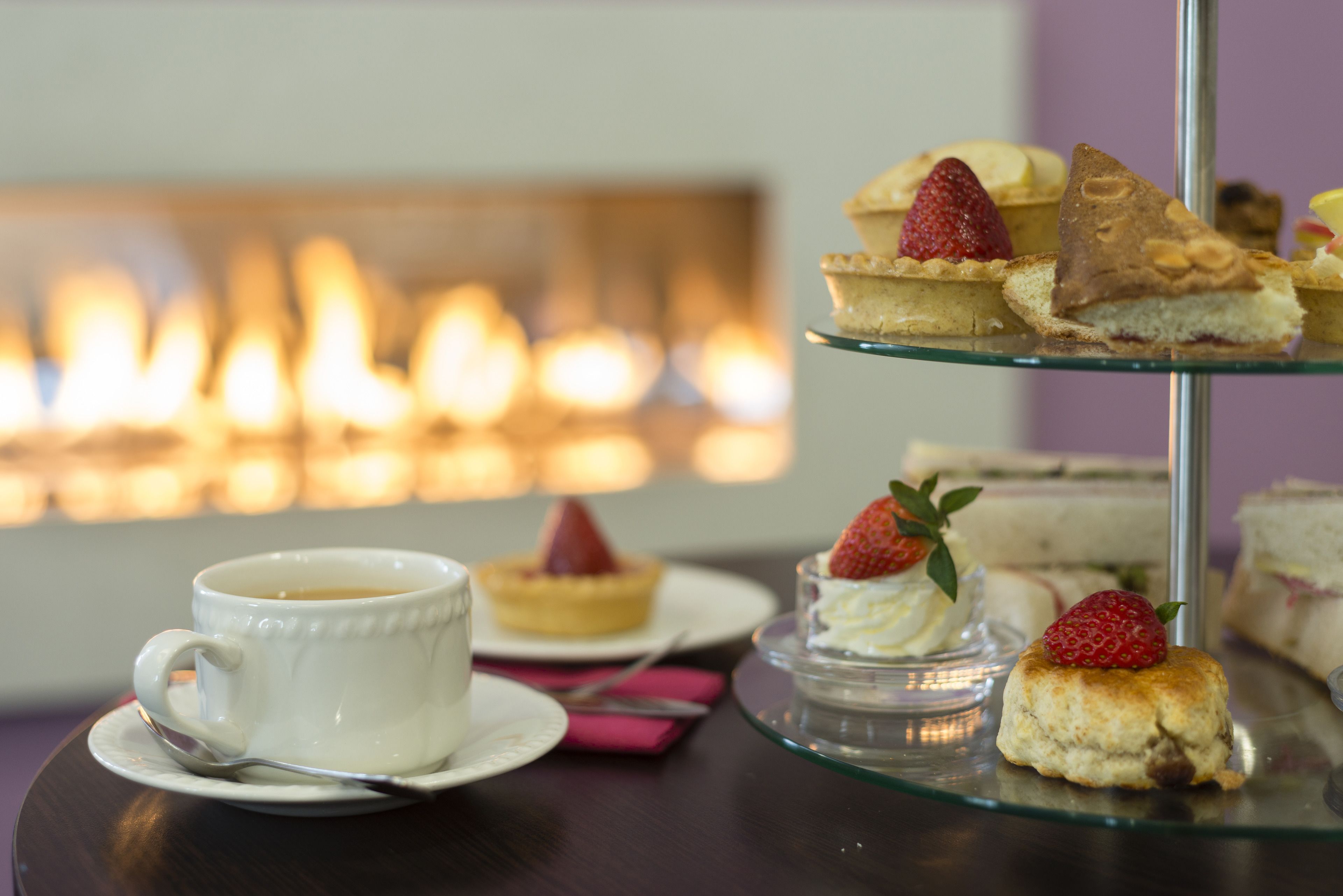 A tiered dessert stand with various pastries and a cup of coffee on a table with a blurred background of lit candles.