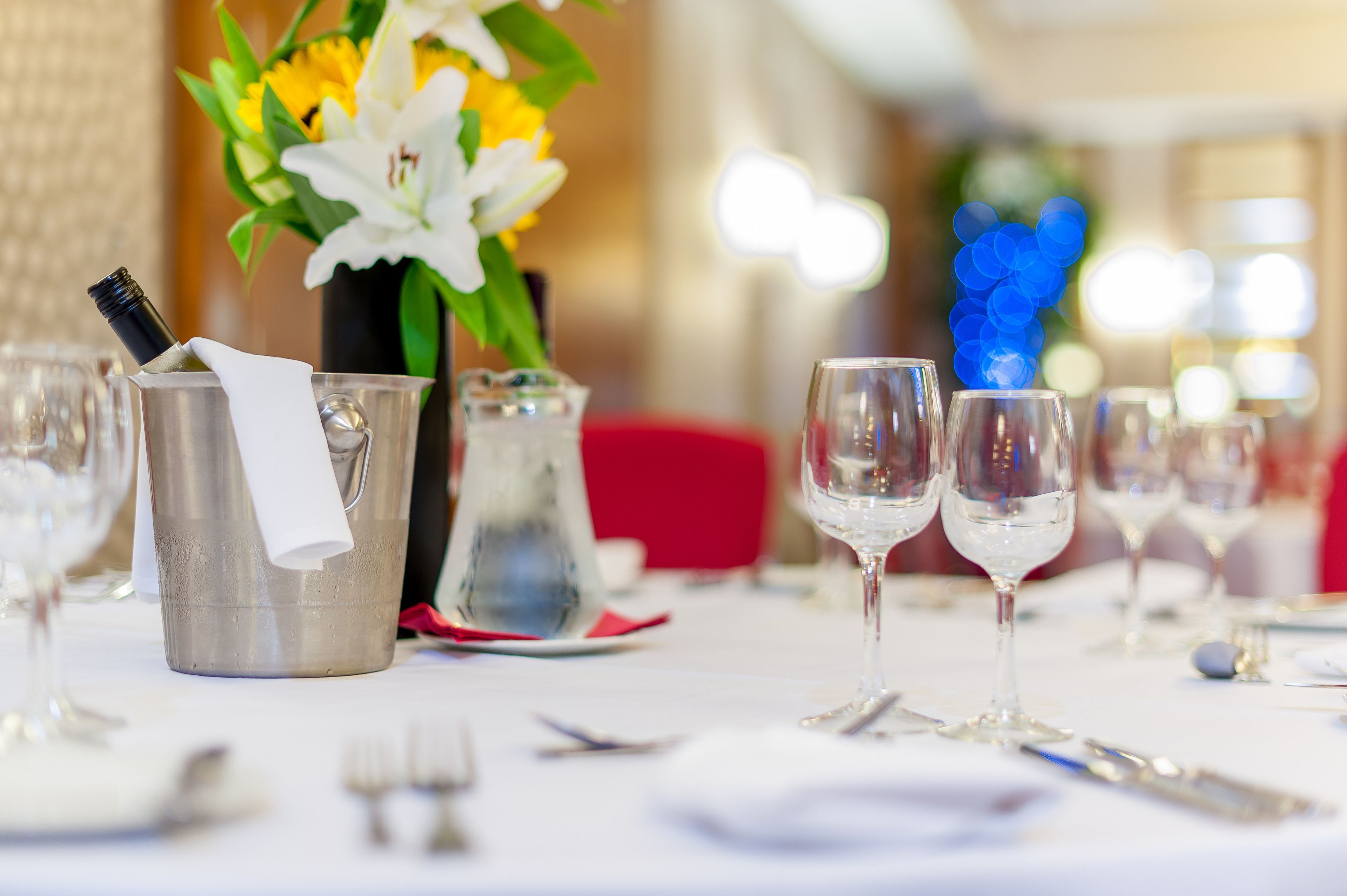 Une table à manger dressée avec des verres à vin, une bouteille de champagne et un vase rempli de fleurs.