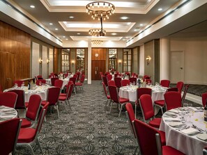 Une salle de banquet avec des tables rondes, des chaises rouges et un tapis à motifs.