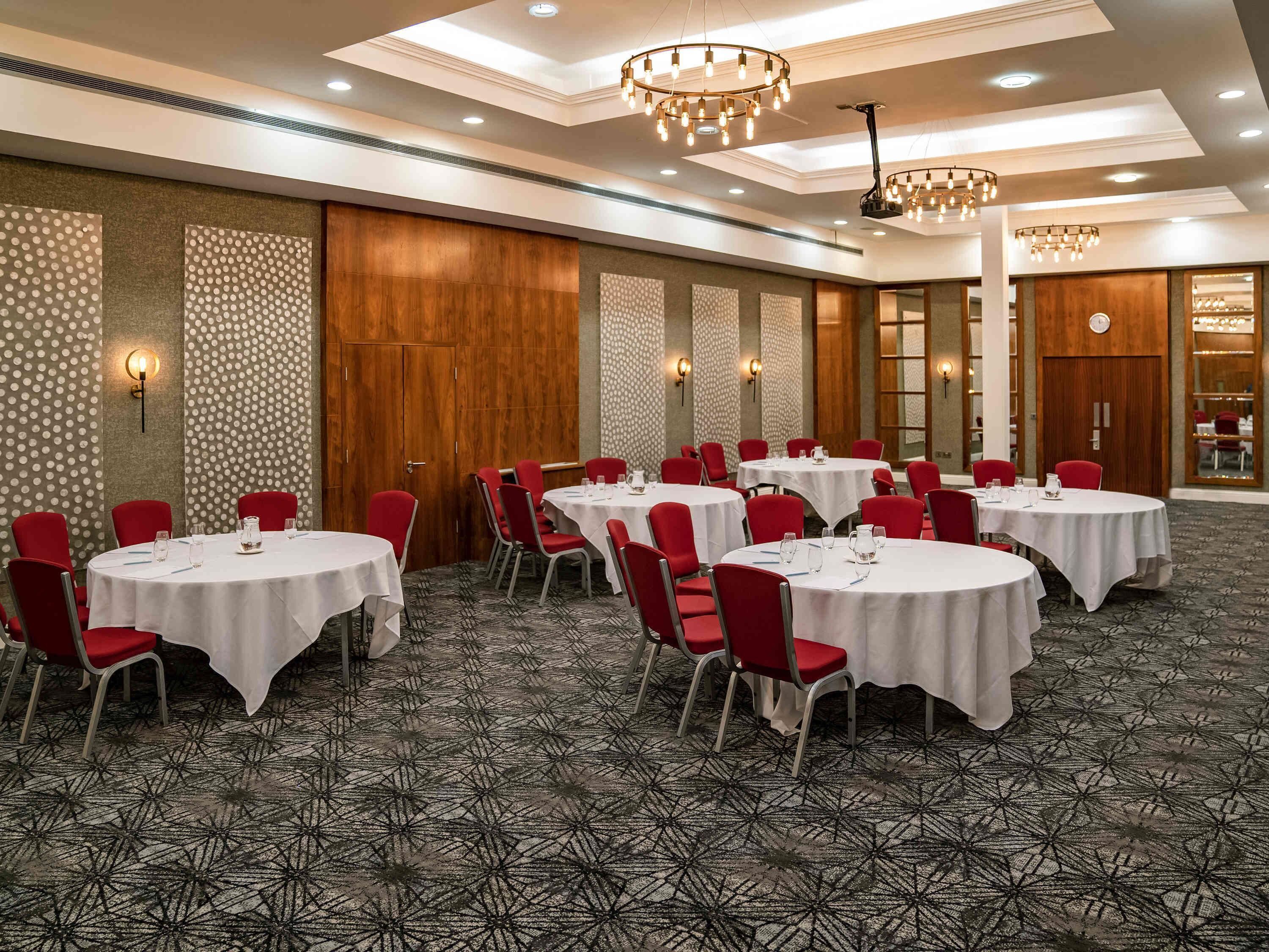 A conference room with round tables, red chairs, and patterned carpet.