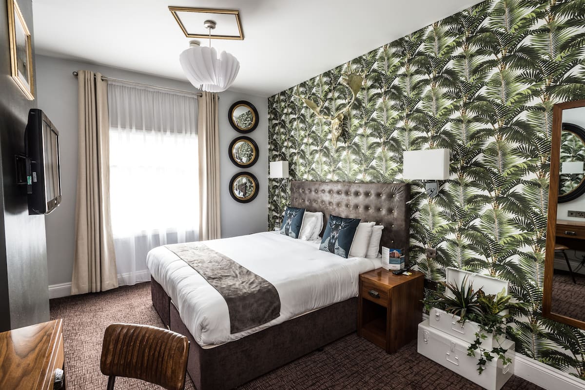 A hotel room with a large bed, a television, a desk, and a mirror.