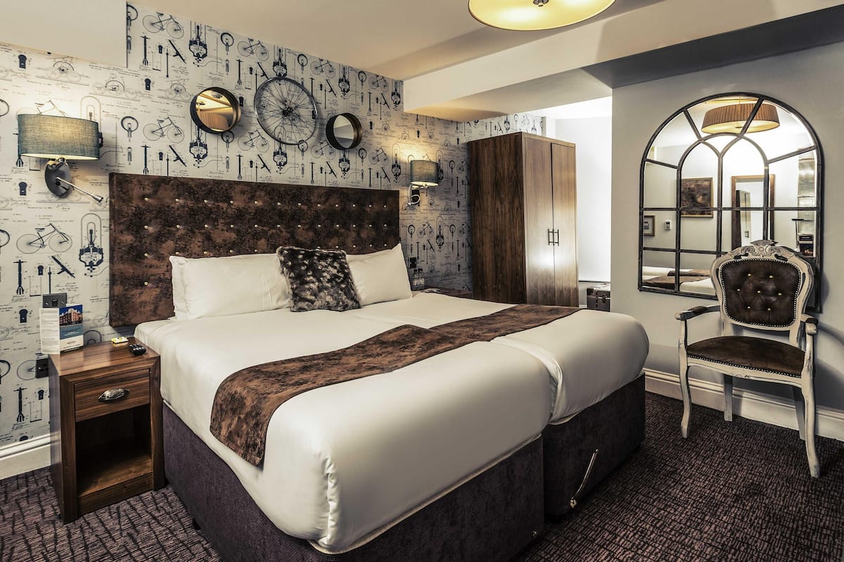 A modern hotel room with a large bed, a wooden headboard, a mirror, and a decorative wall with bicycle illustrations.