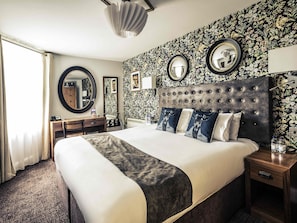 Ein Hotelzimmer mit einem großen Bett, einem Schreibtisch, einem Stuhl, einem Schminktisch und einem Spiegel.