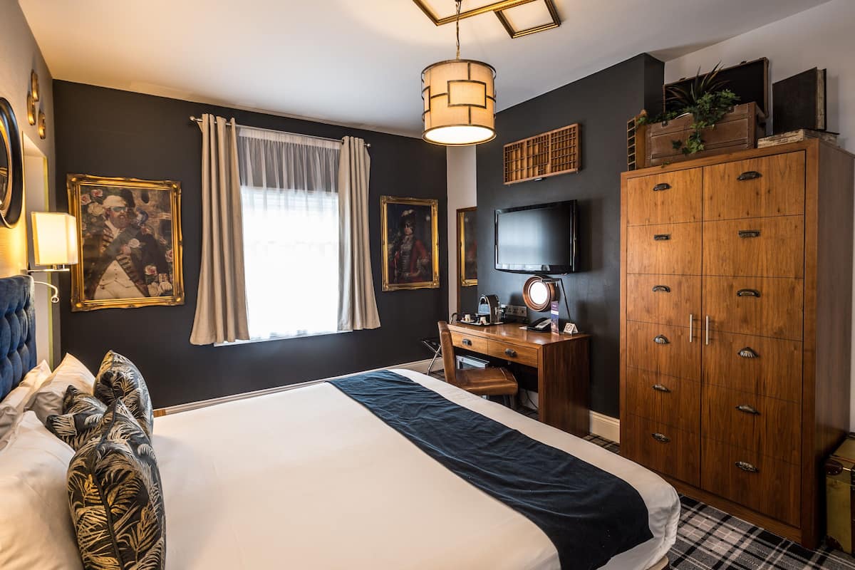 A hotel room with a large bed, a desk, a wardrobe, and a television.