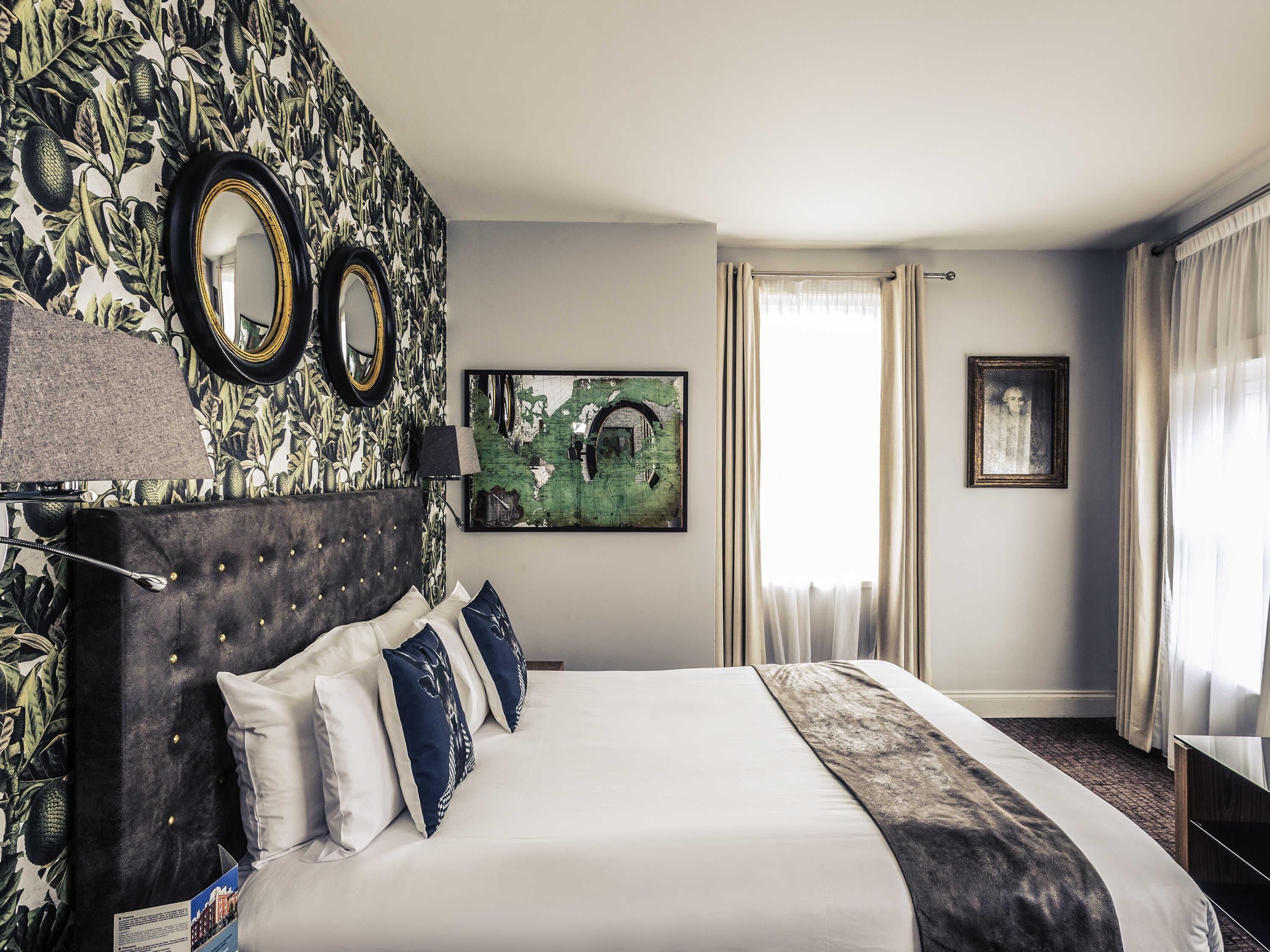 Habitación de hotel con una cama grande, cabecera con botones, un espejo, una obra de arte con un mapa y una fotografía enmarcada en la pared.