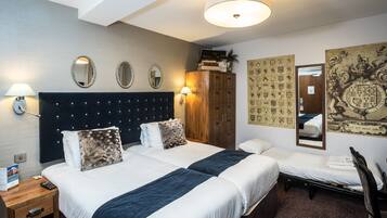A hotel room with two beds, a wooden wardrobe, a mirror, and a wall with decorative panels.