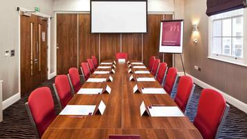 A conference room with a long table, red chairs, a projector screen, and a whiteboard.