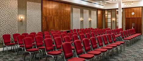 A conference room with rows of red chairs, a patterned carpet, and a ceiling with recessed lighting and chandeliers.