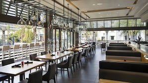 Un restaurante moderno con mesas largas y cabinas, ventanas amplias y lámparas colgantes.