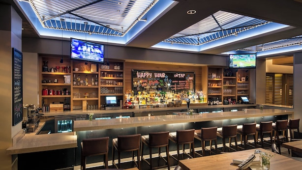 Un bar moderno con techo alto, tragaluces y barra con asientos.