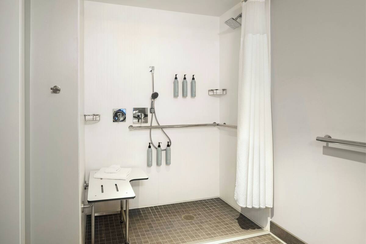 A small, white bathroom with a shower, a sink, and a towel rack.