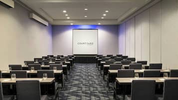 A conference room with rows of tables and chairs, a large screen displaying "COURTYARD BY MARBERT", and a patterned carpet.