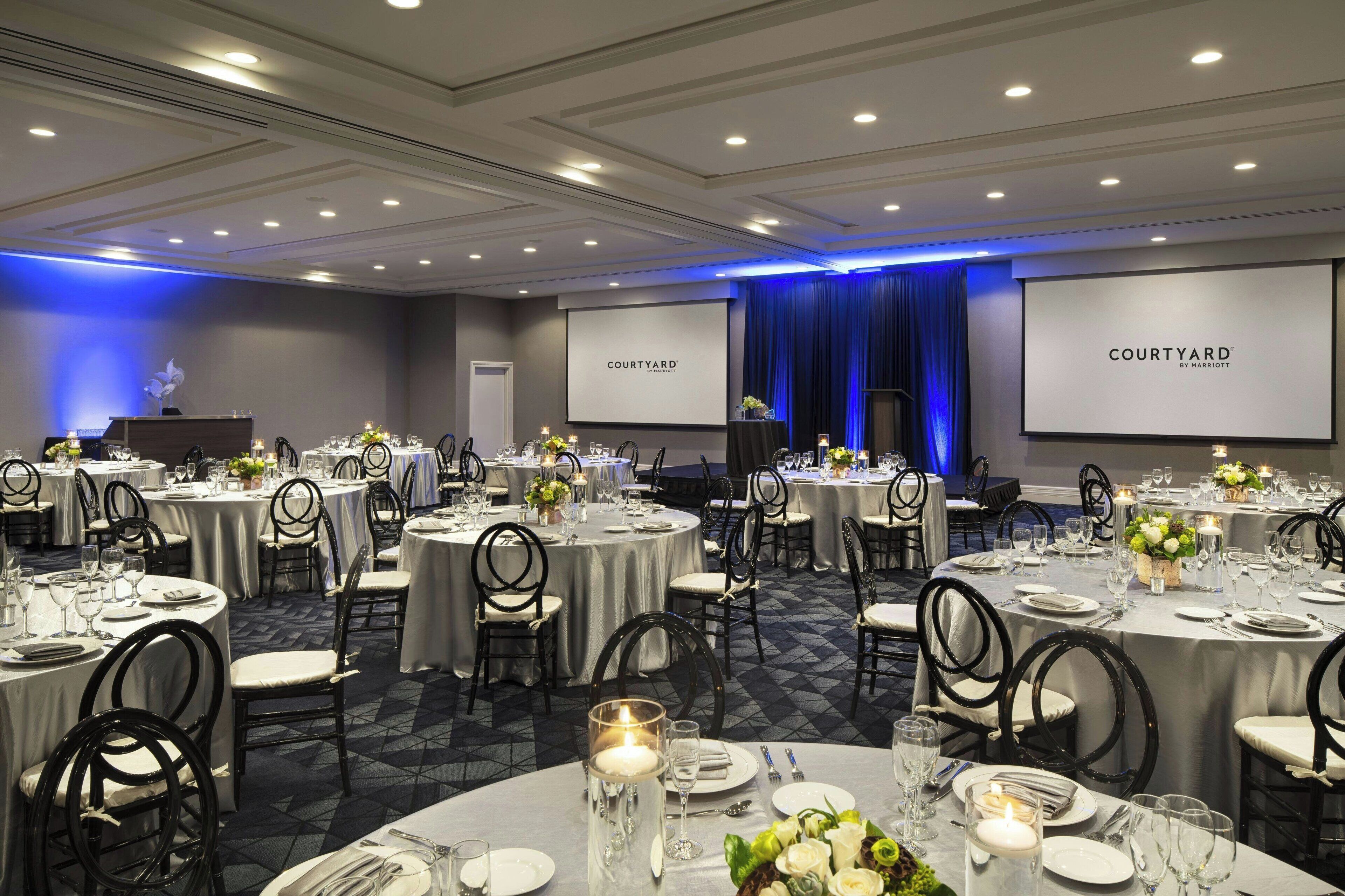 A banquet hall with round tables, chairs, and a large screen displaying "COURTYARD BY MARRIOTT".