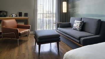 Ein modernes Hotelzimmer mit Ledersessel, grauem Sofa und Couchtisch aus Holz.
