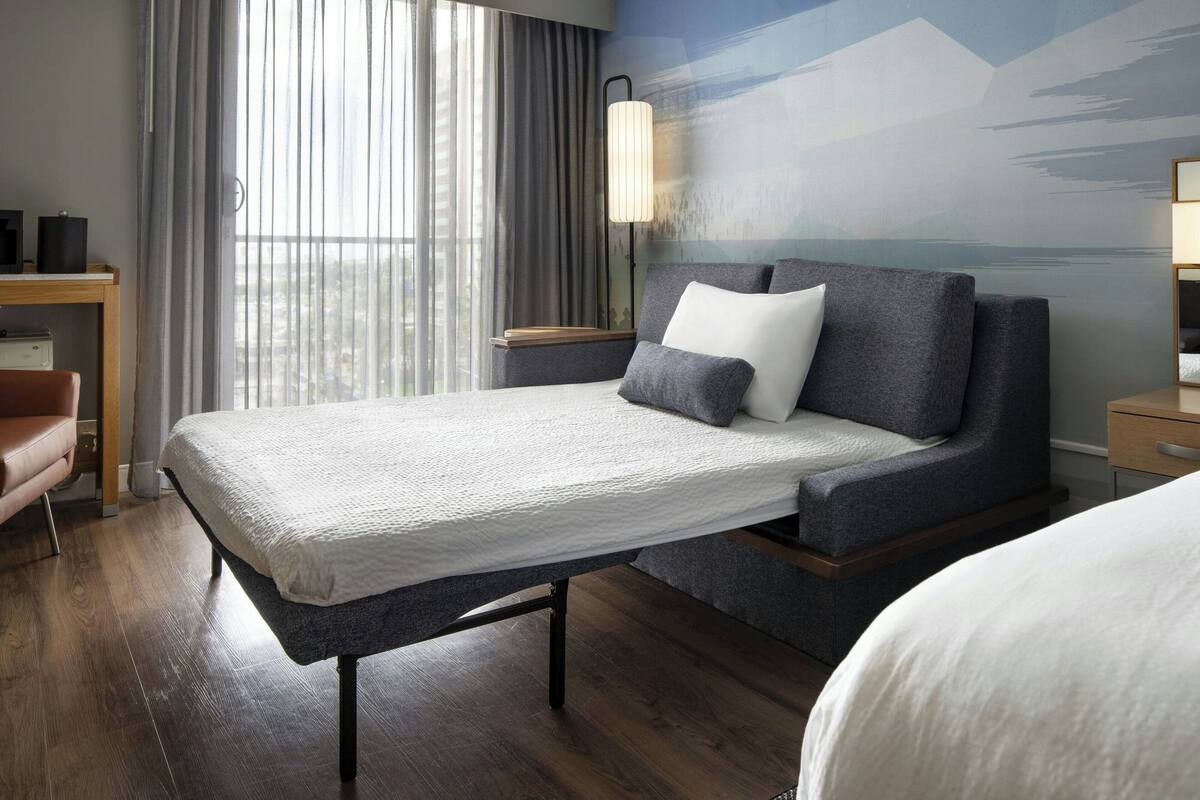 A modern hotel room with a bed, a desk, and a chair.