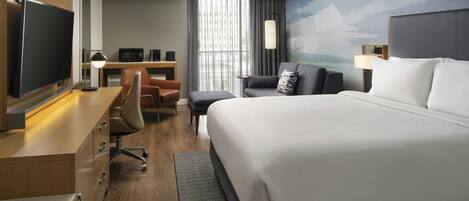 Habitación de hotel con una cama grande, un escritorio con televisor de pantalla plana, un sillón cómodo y vistas a la ciudad desde la ventana.
