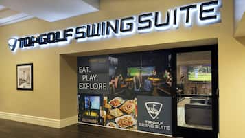 A hotel entrance with a sign for the TopGolf Swing Suite, featuring a golf theme with images of golf courses, food, and a TV screen displaying a golf game.