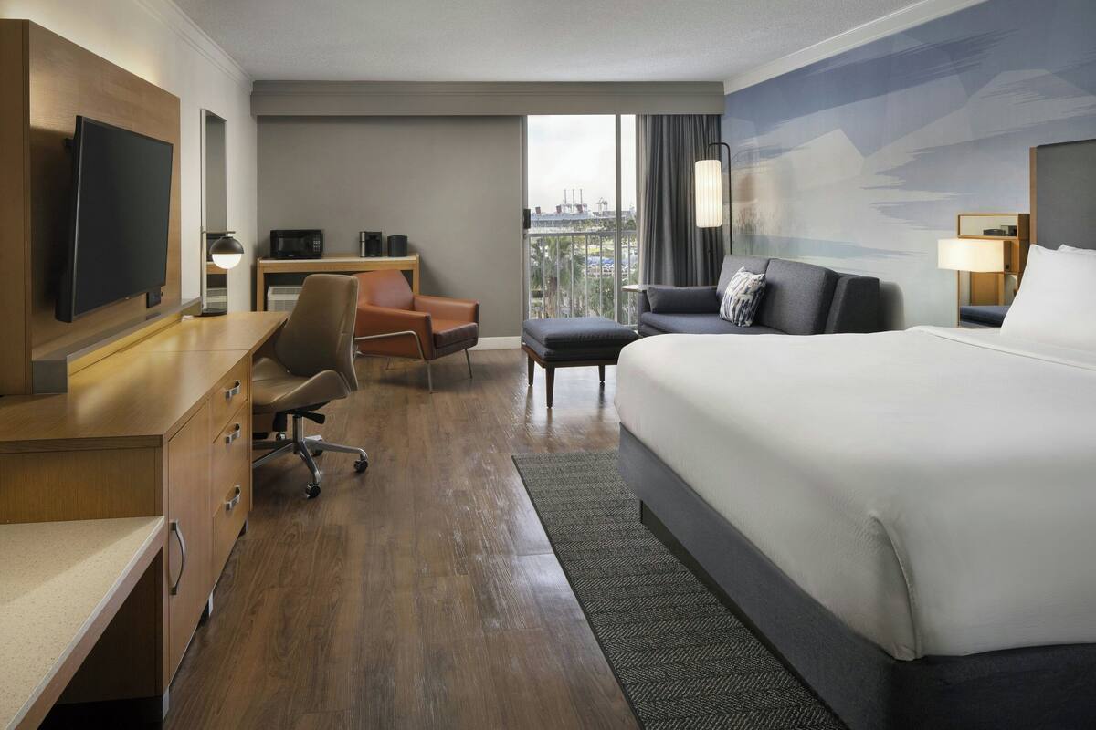 A hotel room with a bed, desk, chair, and a TV.