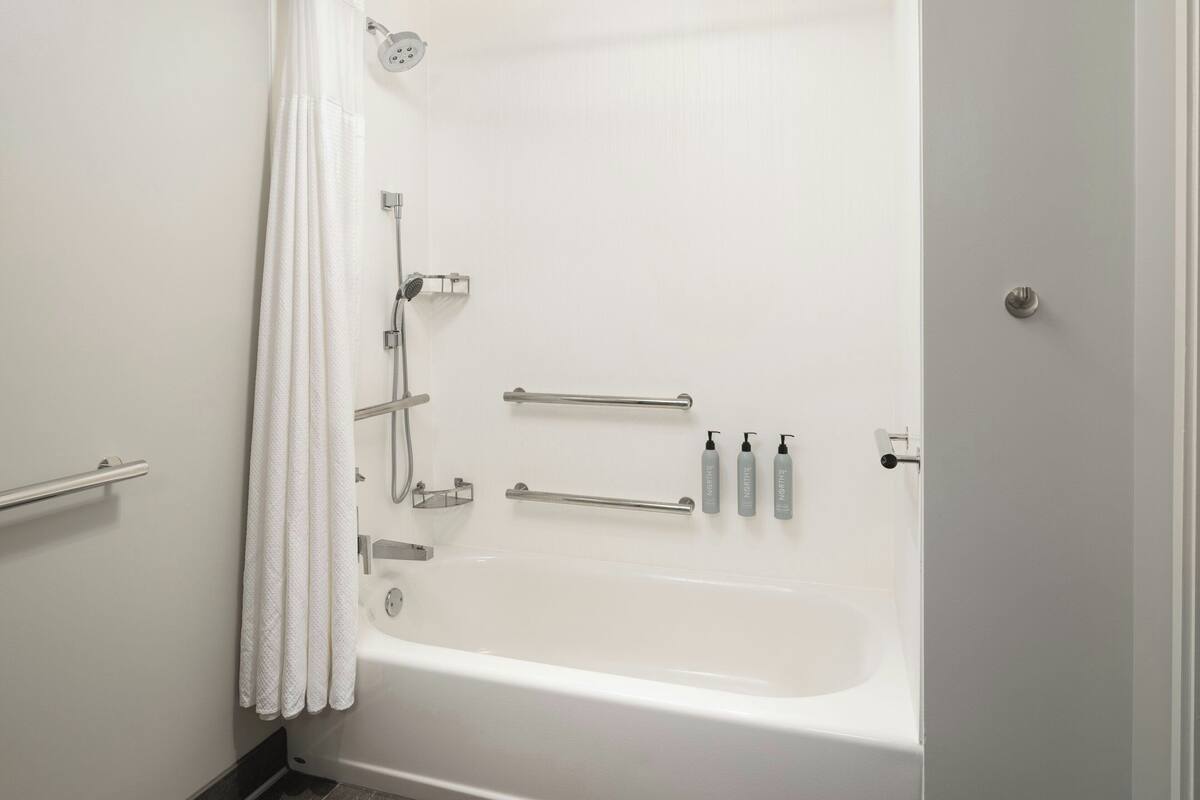A white bathtub with grab bars, a showerhead, and a towel rack.