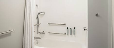 A white bathtub with grab bars, a showerhead, and a towel rack.