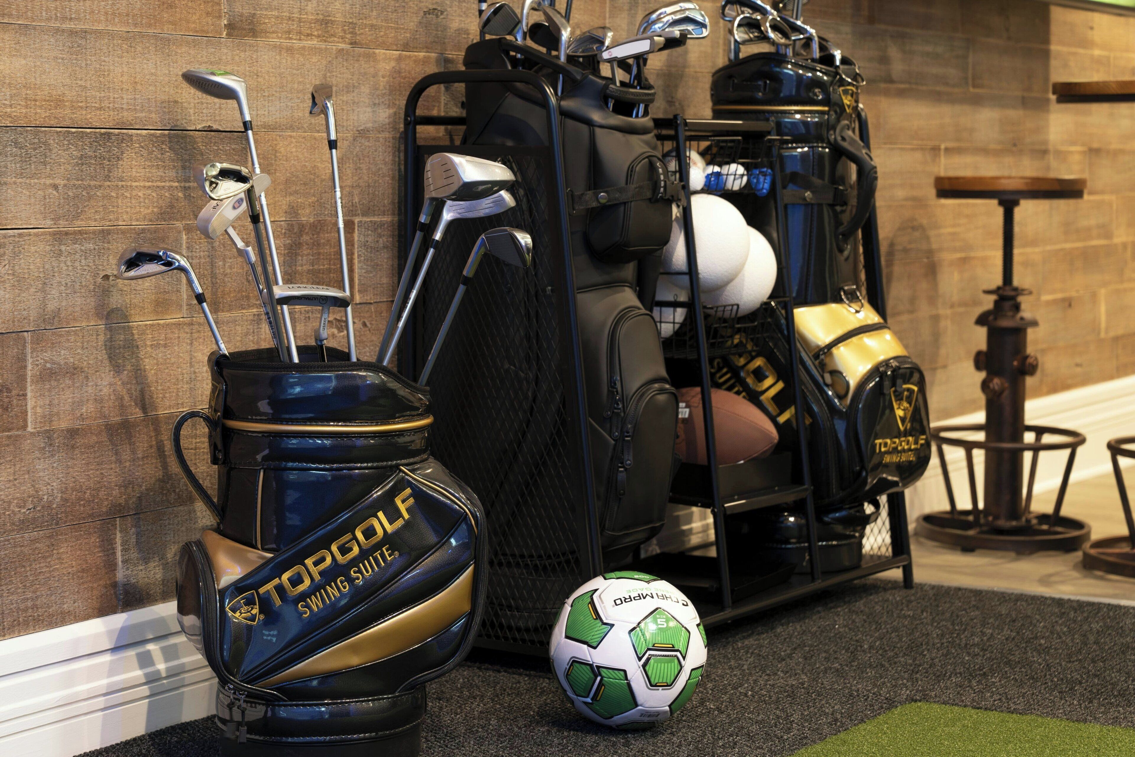 Un bolso de golf con un traje de entrenamiento para swing y un balón de fútbol sobre un piso alfombrado.
